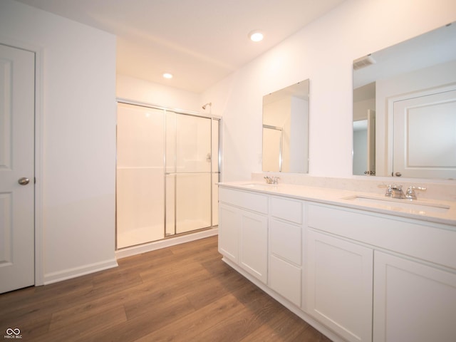 full bath featuring double vanity, a shower stall, a sink, and wood finished floors