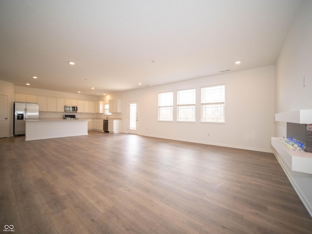 unfurnished living room featuring baseboards, dark wood-type flooring, and recessed lighting