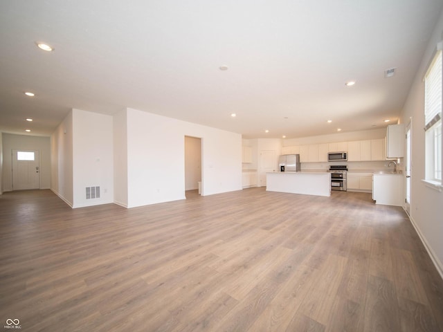 unfurnished living room with visible vents, baseboards, light wood-style floors, a sink, and recessed lighting