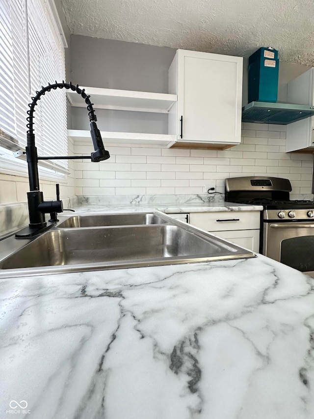 kitchen featuring white cabinetry, decorative backsplash, gas range, wall chimney range hood, and a textured ceiling