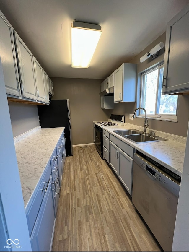 kitchen with sink, light hardwood / wood-style floors, gas stove, black fridge, and stainless steel dishwasher