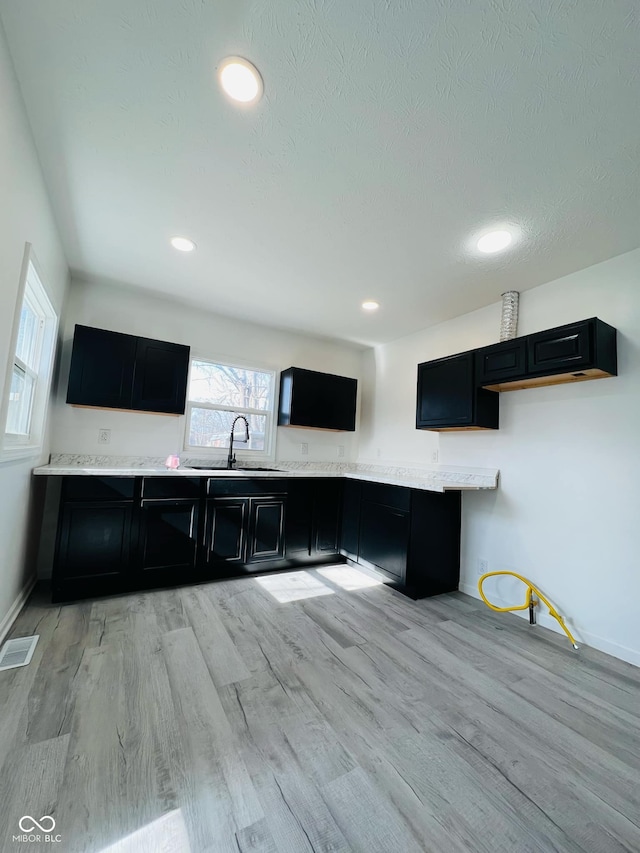 kitchen with sink, light hardwood / wood-style floors, a textured ceiling, and light stone countertops