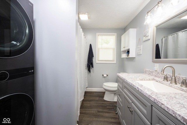 bathroom featuring wood-type flooring, stacked washer and dryer, vanity, toilet, and a textured ceiling