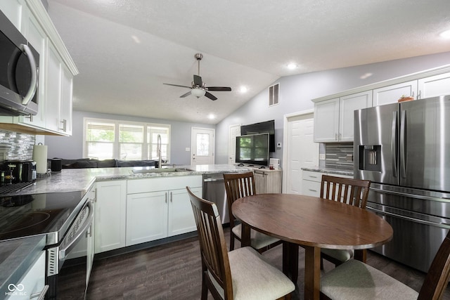 kitchen with vaulted ceiling, appliances with stainless steel finishes, sink, white cabinets, and light stone countertops