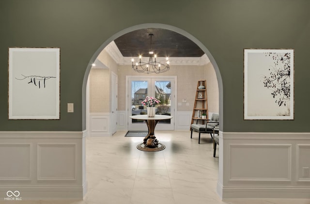 hall with arched walkways, a decorative wall, marble finish floor, wainscoting, and an inviting chandelier