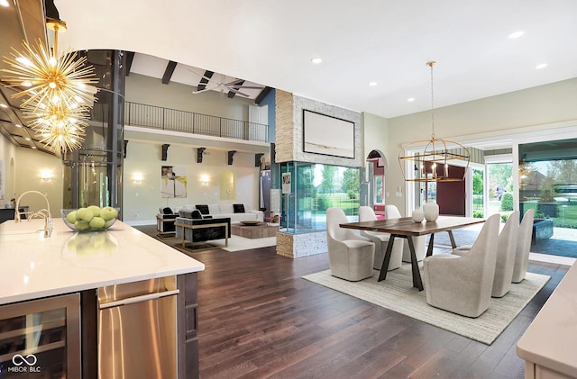 kitchen with a towering ceiling, wine cooler, open floor plan, dark wood-style flooring, and an inviting chandelier