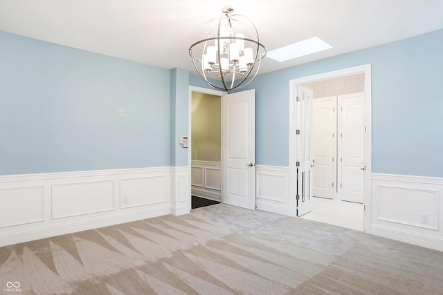 unfurnished room with a skylight, a chandelier, carpet flooring, and wainscoting