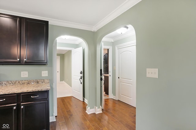 hallway with dark wood-style floors, arched walkways, ornamental molding, and baseboards