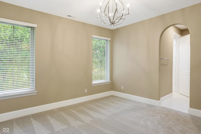 spare room with arched walkways, light colored carpet, visible vents, an inviting chandelier, and baseboards