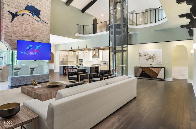 living room featuring arched walkways, a wainscoted wall, dark wood-type flooring, beamed ceiling, and a decorative wall