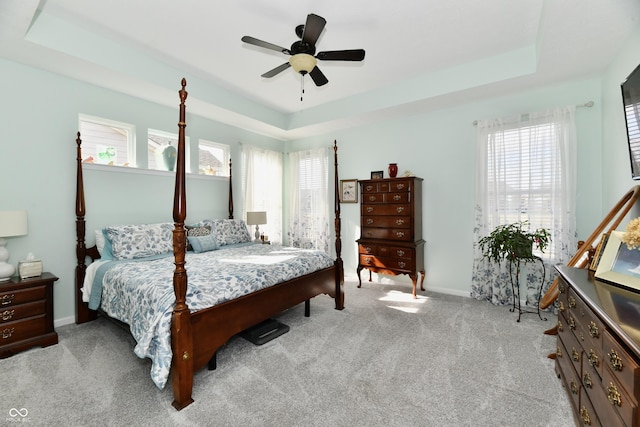 carpeted bedroom with a raised ceiling and ceiling fan