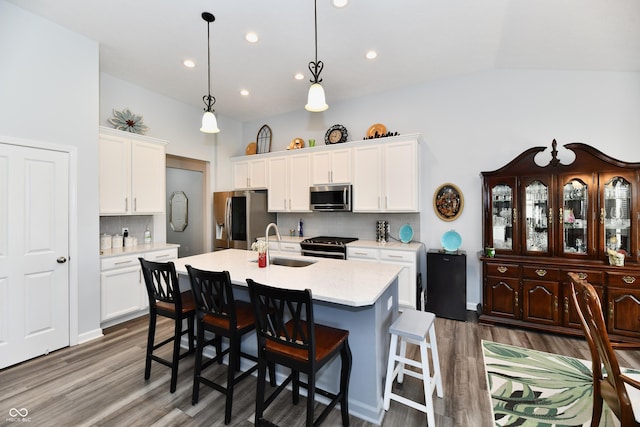 kitchen featuring sink, white cabinets, hanging light fixtures, stainless steel appliances, and a center island with sink