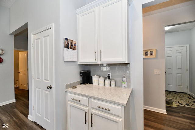 bar with light stone countertops, dark hardwood / wood-style floors, white cabinets, and backsplash