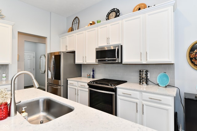 kitchen featuring sink, white cabinetry, stainless steel appliances, light stone countertops, and decorative backsplash