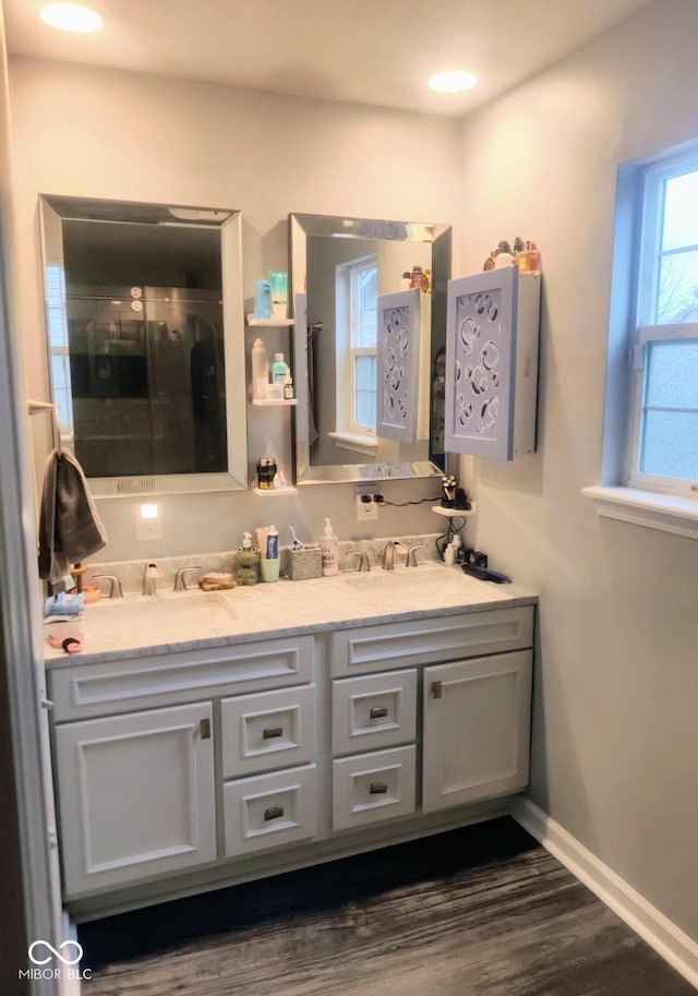 full bathroom with double vanity, wood finished floors, a sink, and baseboards