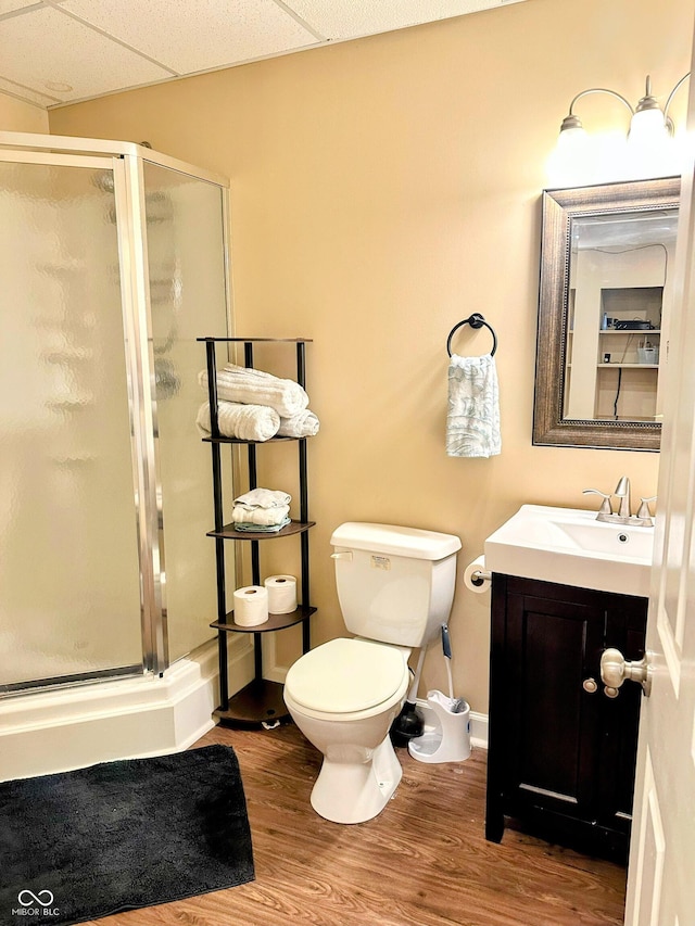 full bathroom featuring toilet, a paneled ceiling, wood finished floors, vanity, and a stall shower