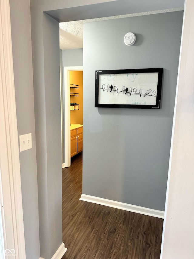 hallway featuring dark wood-style floors, a textured ceiling, and baseboards