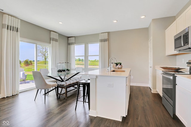 kitchen with appliances with stainless steel finishes, white cabinetry, an island with sink, sink, and a breakfast bar area