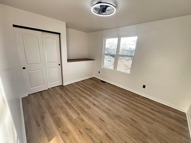 unfurnished bedroom featuring baseboards, a closet, visible vents, and wood finished floors