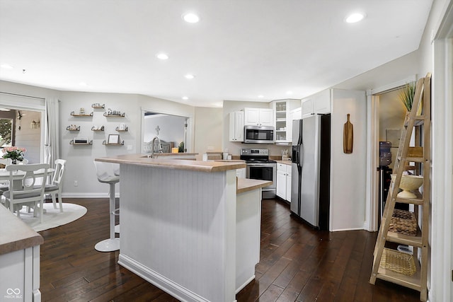 kitchen with a breakfast bar area, appliances with stainless steel finishes, white cabinets, a kitchen island, and dark hardwood / wood-style flooring