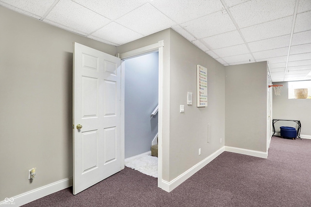 hallway featuring a paneled ceiling and dark colored carpet