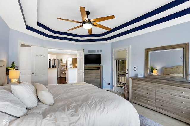 carpeted bedroom with ceiling fan, stainless steel fridge, and a raised ceiling