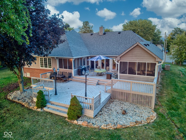 rear view of property featuring a wooden deck, central air condition unit, a sunroom, and a lawn