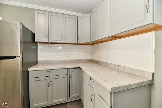 kitchen with dark wood-type flooring, stainless steel fridge, gray cabinets, light stone countertops, and decorative backsplash