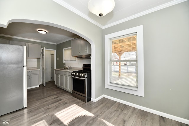 kitchen featuring crown molding, hardwood / wood-style flooring, gray cabinetry, stainless steel appliances, and tasteful backsplash