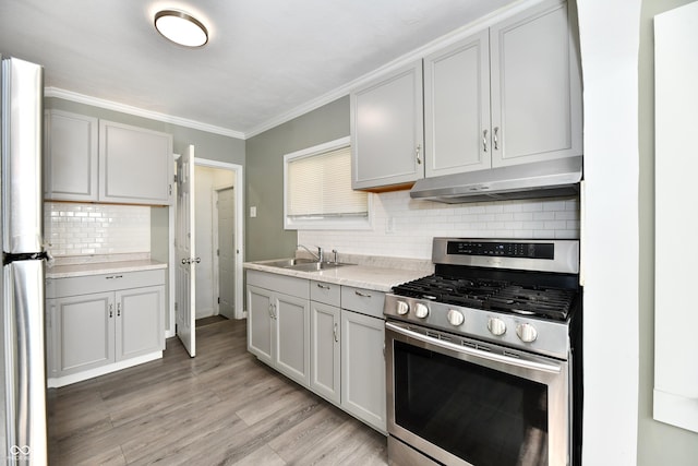 kitchen with sink, decorative backsplash, ornamental molding, stainless steel appliances, and light wood-type flooring