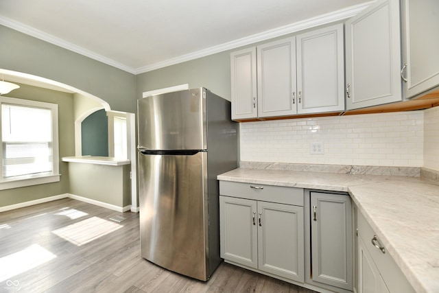 kitchen with gray cabinetry, tasteful backsplash, light hardwood / wood-style flooring, ornamental molding, and stainless steel fridge