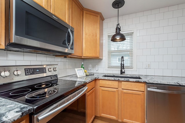 kitchen with sink, tasteful backsplash, light stone counters, appliances with stainless steel finishes, and pendant lighting