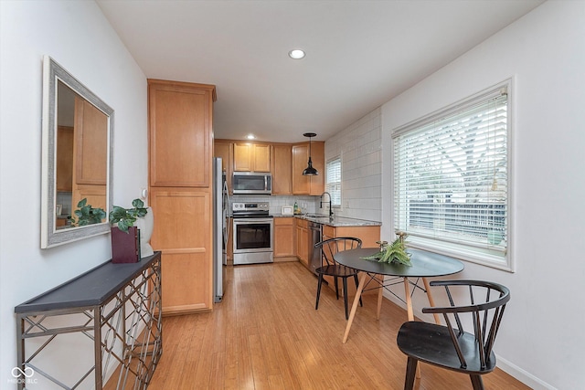 kitchen featuring pendant lighting, decorative backsplash, stainless steel appliances, light stone countertops, and light hardwood / wood-style flooring