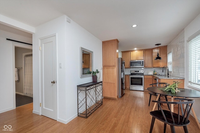 kitchen featuring stainless steel appliances, pendant lighting, decorative backsplash, and light hardwood / wood-style flooring