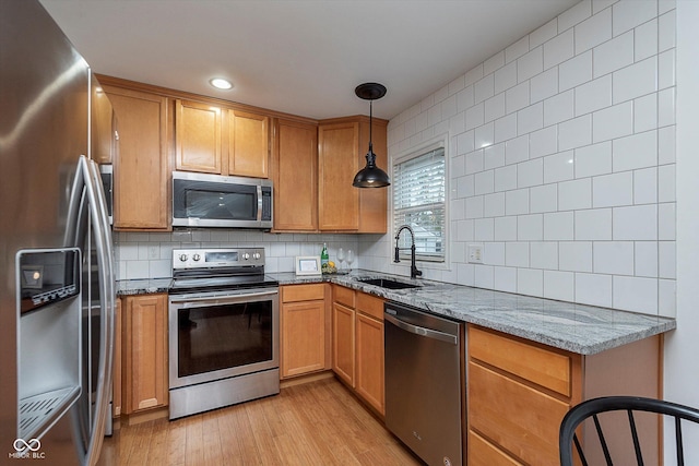 kitchen with sink, tasteful backsplash, pendant lighting, stainless steel appliances, and light stone countertops