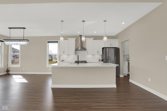 kitchen with white cabinetry, wall chimney range hood, decorative light fixtures, and an island with sink