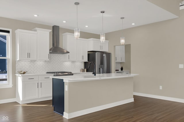 kitchen featuring white cabinetry, wall chimney exhaust hood, stainless steel fridge, and a center island with sink