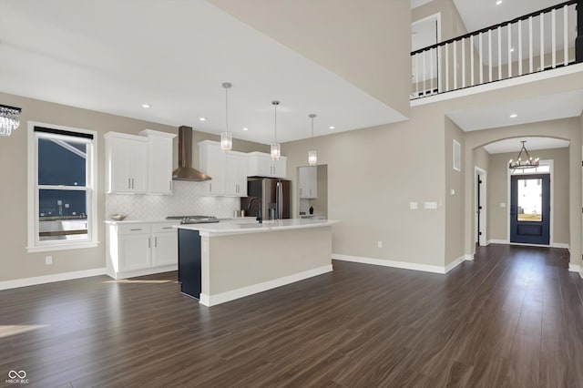 kitchen with pendant lighting, stainless steel fridge, an island with sink, white cabinets, and wall chimney exhaust hood