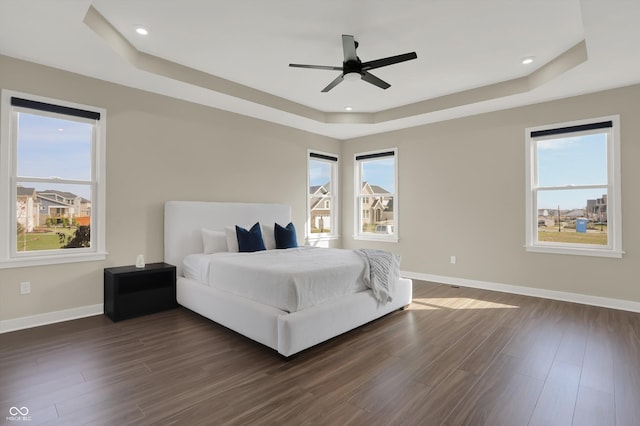 bedroom with a tray ceiling, dark hardwood / wood-style flooring, and multiple windows