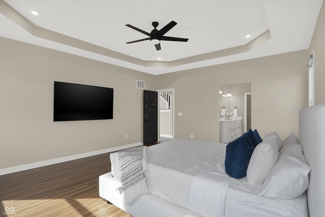 bedroom featuring hardwood / wood-style flooring, ceiling fan, ensuite bathroom, and a tray ceiling