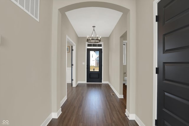 foyer featuring dark wood-style floors, arched walkways, a notable chandelier, visible vents, and baseboards