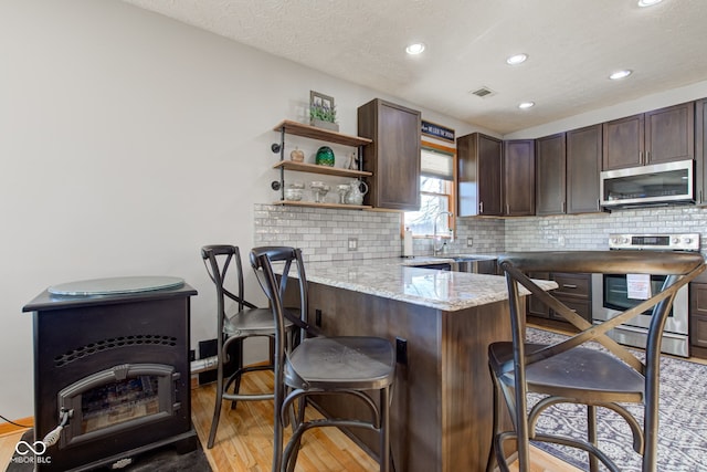 kitchen with a breakfast bar, a sink, a peninsula, appliances with stainless steel finishes, and dark brown cabinets