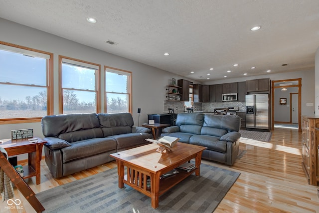 living area featuring light wood finished floors, visible vents, recessed lighting, and a textured ceiling