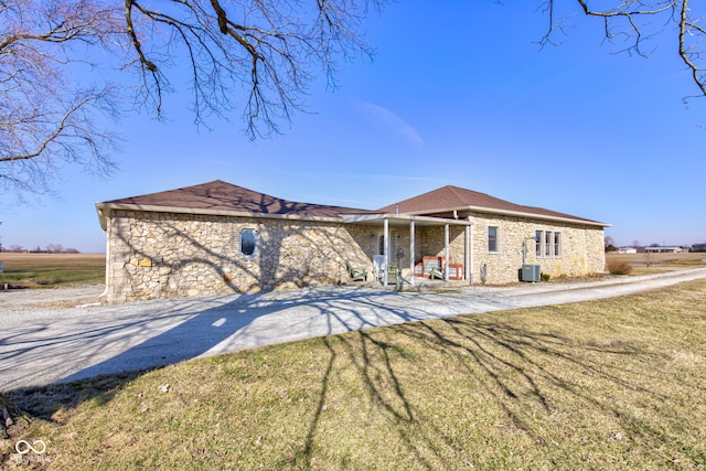 view of front of property with central AC unit, driveway, a front lawn, stone siding, and a patio area