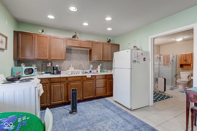 kitchen with tasteful backsplash, white appliances, brown cabinetry, light countertops, and light tile patterned floors