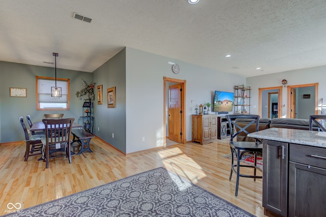 dining space featuring visible vents, a textured ceiling, light wood-type flooring, and baseboards