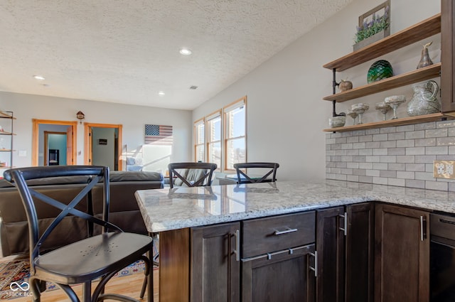 kitchen with open shelves, open floor plan, a peninsula, decorative backsplash, and dark brown cabinets