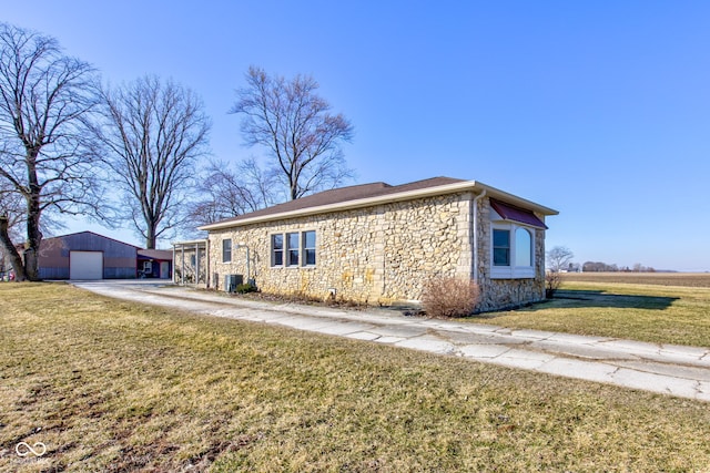 view of front of home featuring central air condition unit, an outbuilding, stone siding, a detached garage, and a front yard