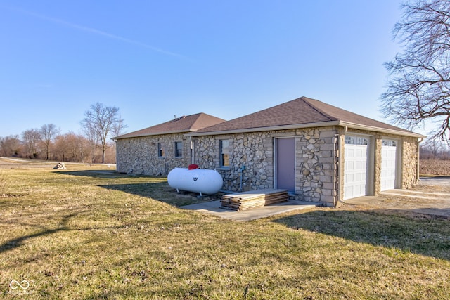 rear view of property with a yard, stone siding, a garage, and a shingled roof