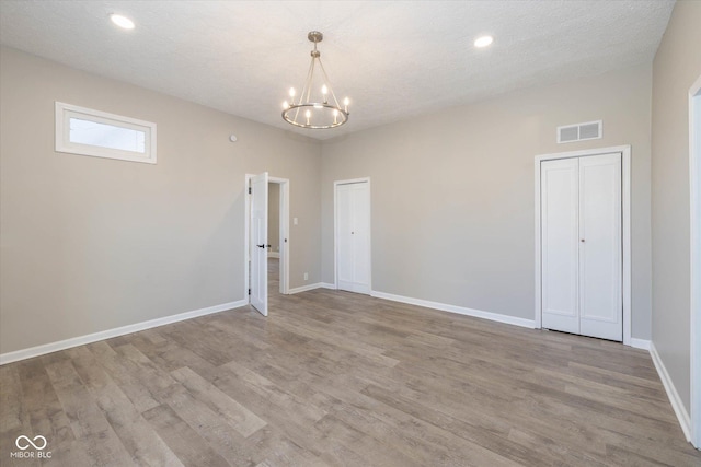 unfurnished room with a chandelier, light hardwood / wood-style flooring, and a textured ceiling